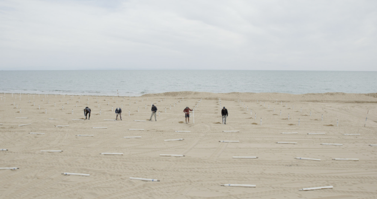 Eine Reihe von Menschen beim Aufstellen von Sonnenschirmen im Dokumentarfilm Vista Mare