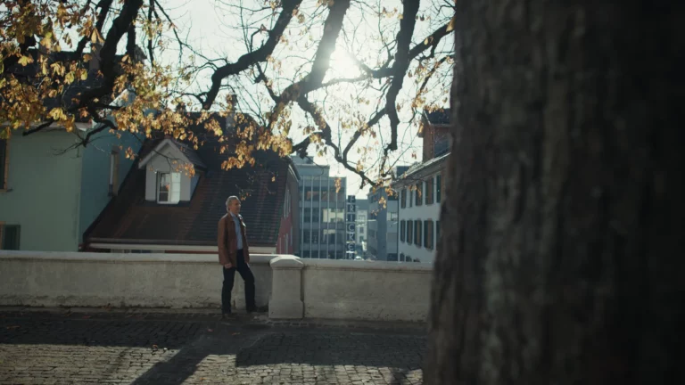 Florian Serex geht über eine erhöhte städtische Terrasse, eingerahmt von einem kahlen Baum im Herbstlicht.